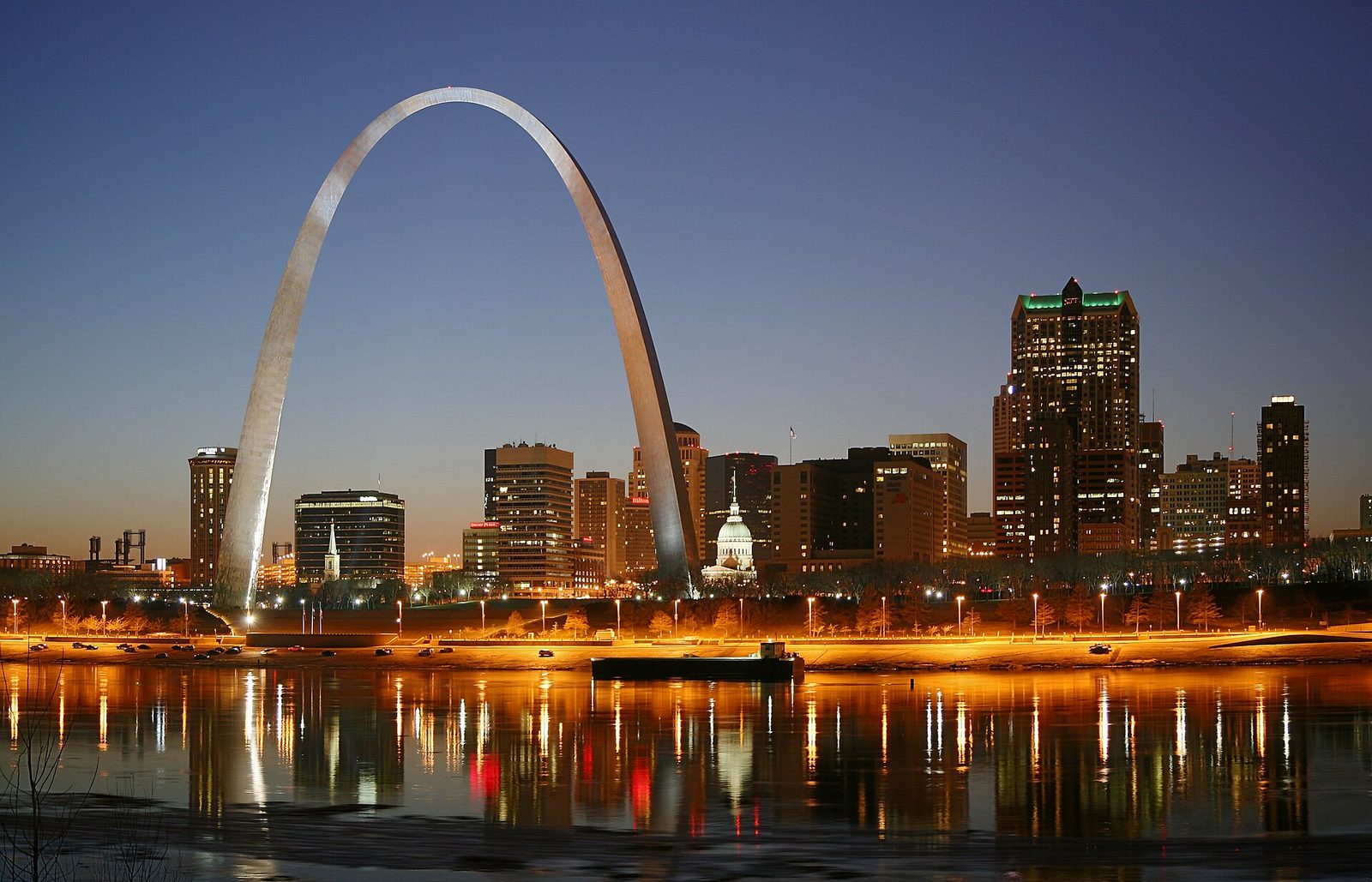 The Gateway Arch and the downtown St. Louis skyline at dusk, reflected in the Mississippi River
